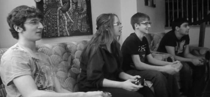 Four lovely humans enjoying some smash on a couch in black and white.